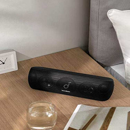 Bluetooth subwoofer speaker on a wooden table near a sofa.