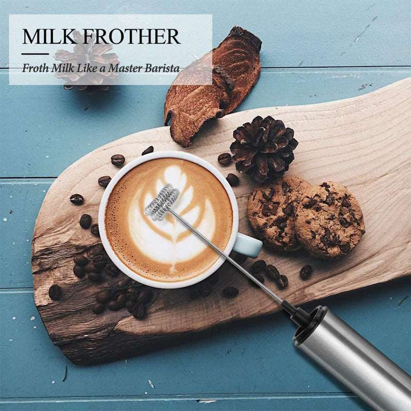 Handheld electric milk frother and egg beater on wooden board with coffee and cookies.